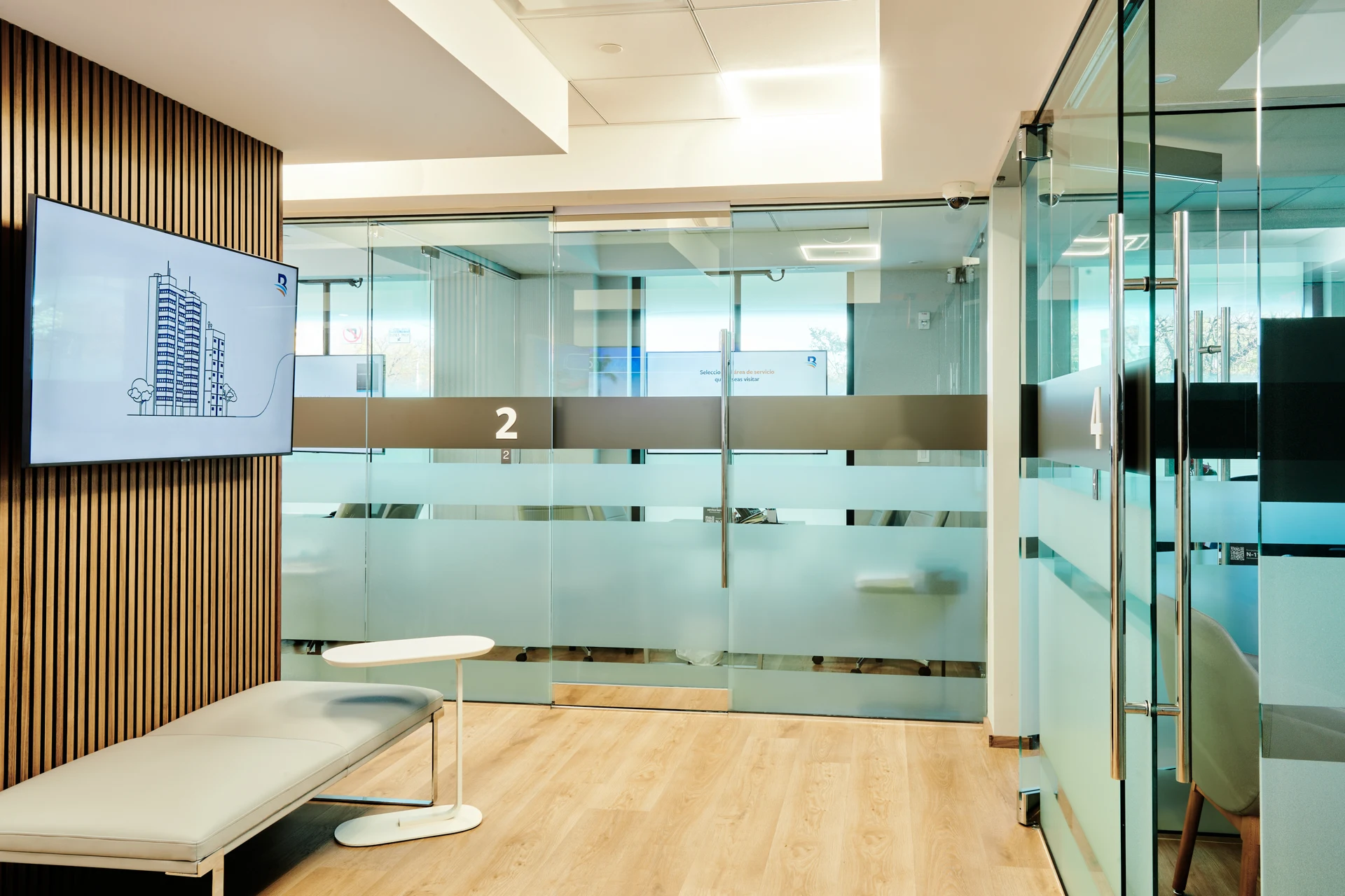 Banreservas: Glass office partitions with frosted bands beside a bench and wood-slat wall