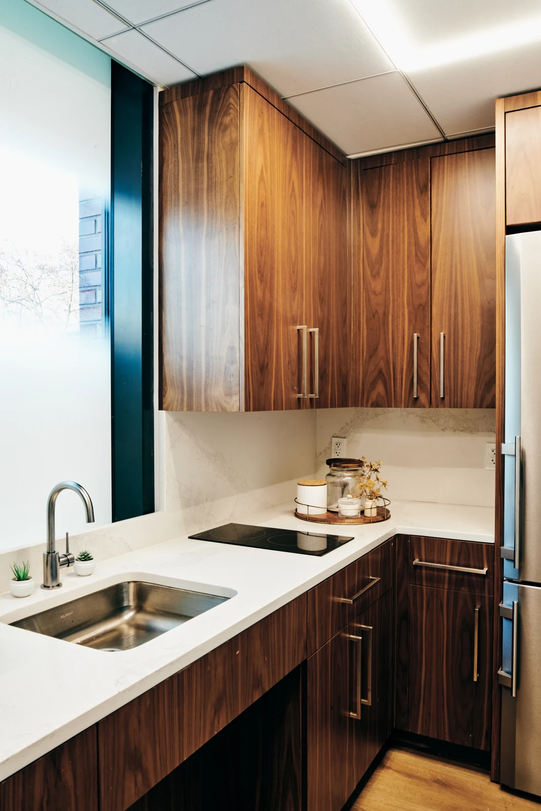 Banreservas: Compact kitchenette with wood cabinetry, white counters, a sink and cooktop