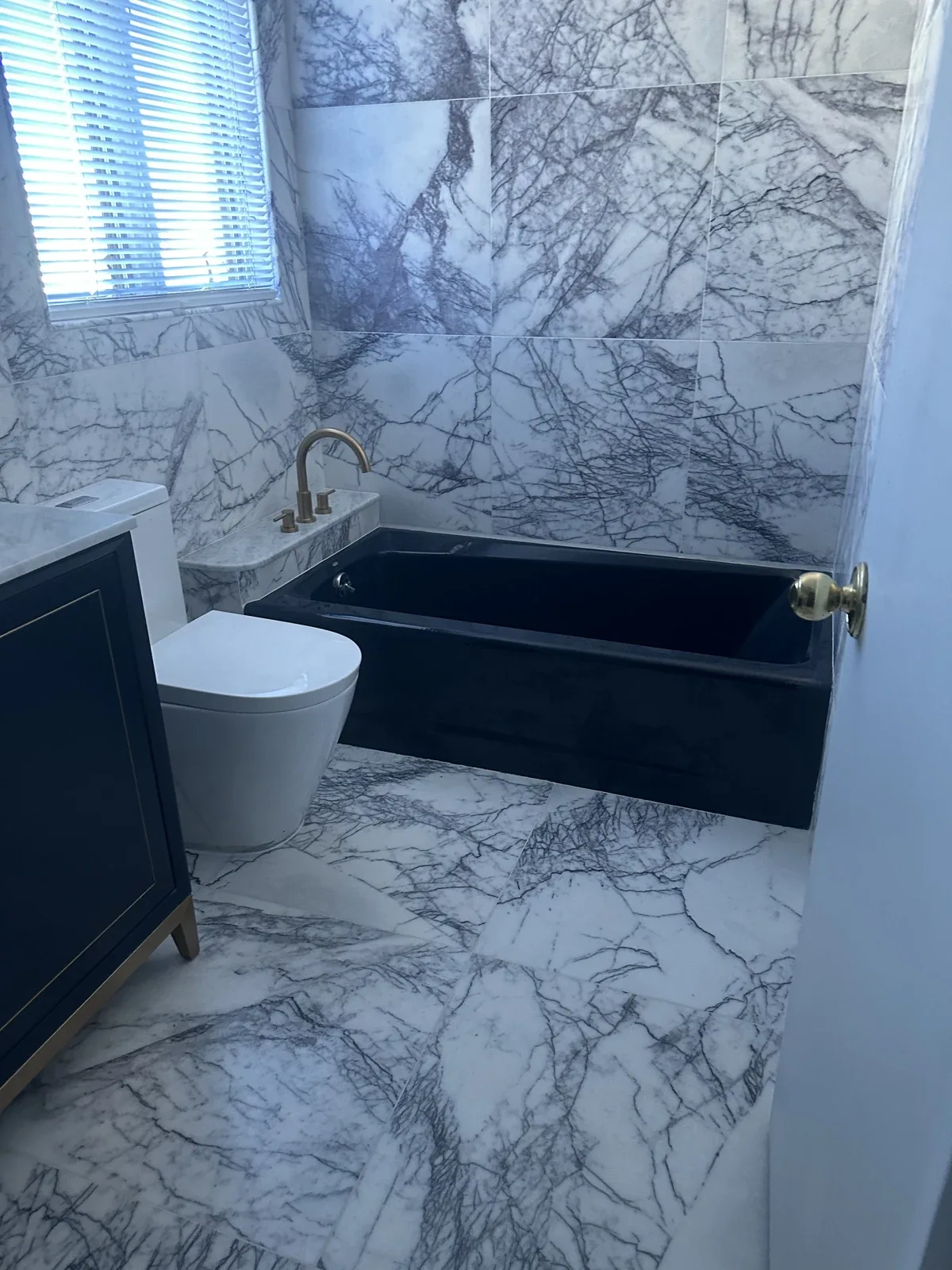 Residential Interiors: Bathroom with a dark bathtub and heavily veined wall and floor tiles