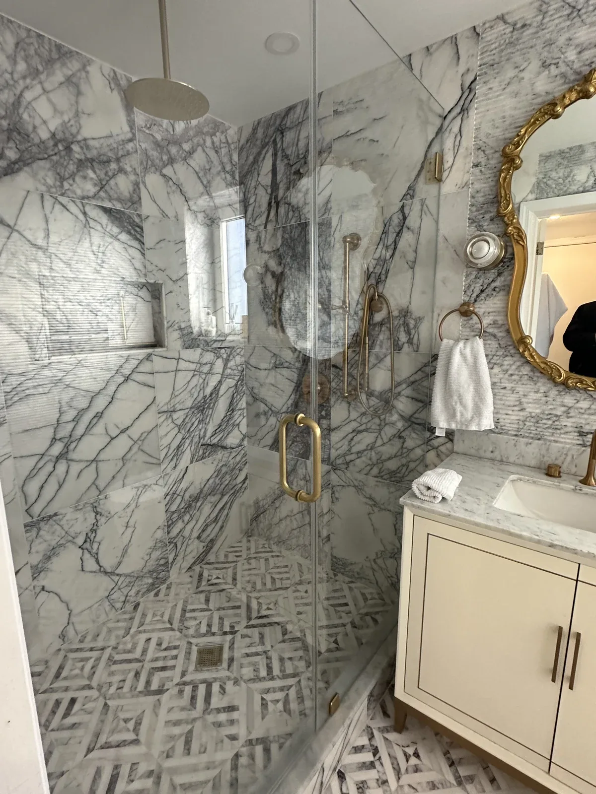 Residential Interiors: Glass-enclosed shower with veined tile, patterned flooring and brass-toned fixtures