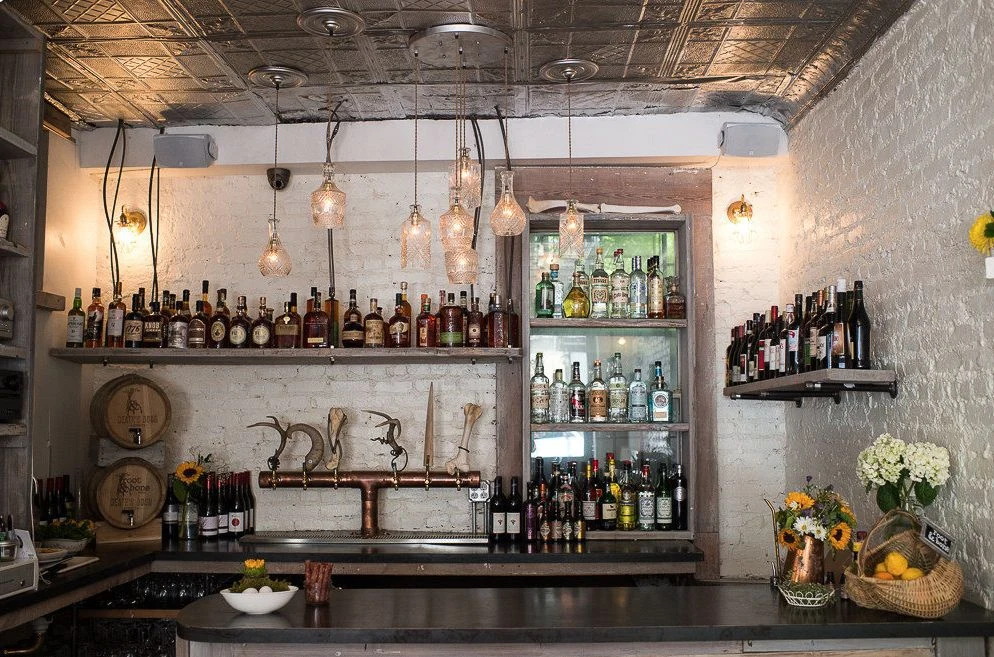 Root & Bone: Bar counter with bottle shelves, pendant lights and white brick walls