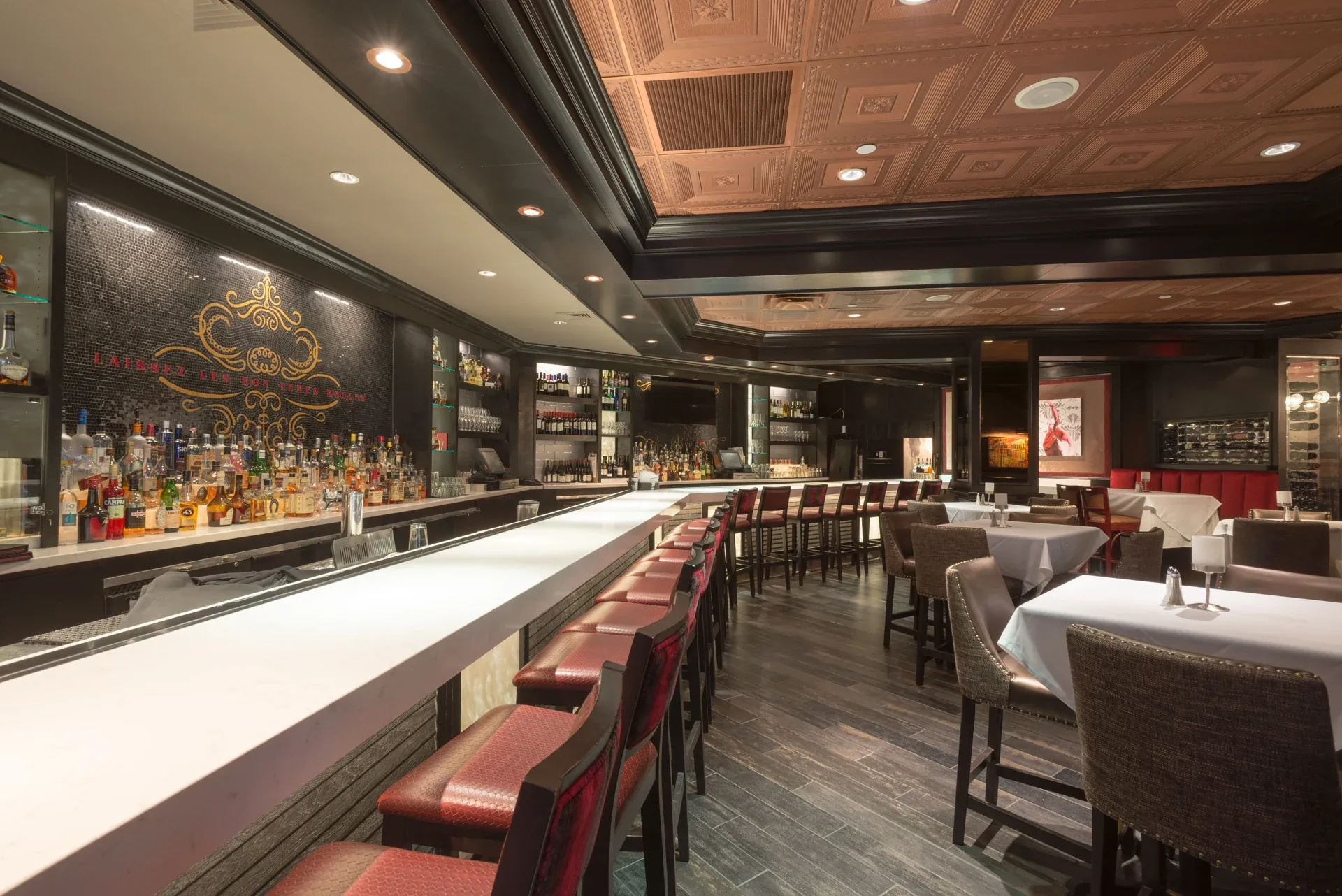 Ruth’s Chris Steakhouse: Long bar with red stools, illuminated bottle shelves and decorative ceiling panels