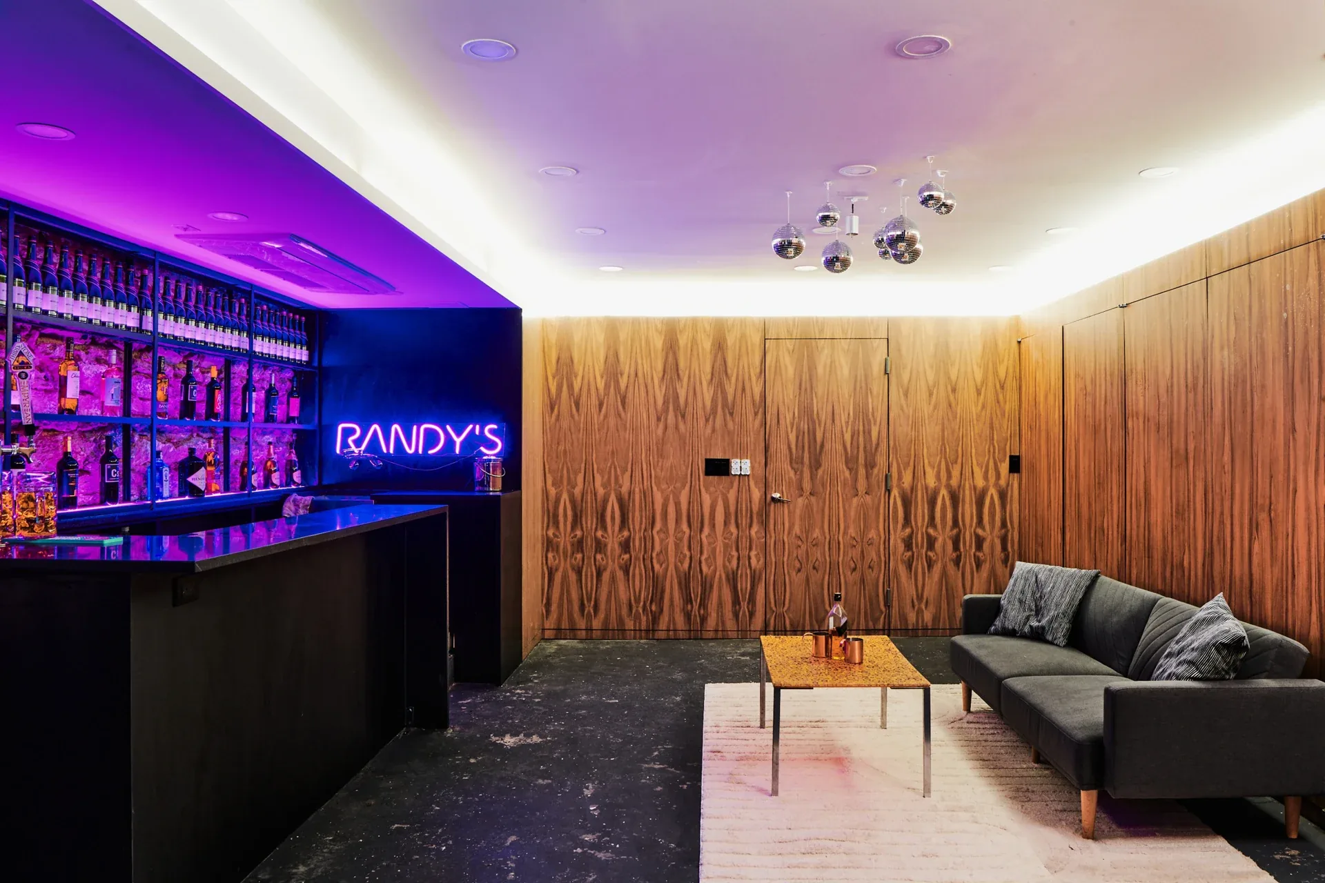 Sigma Nu Fraternity: Lounge with wood-paneled walls, gray sofa and purple-lit bar