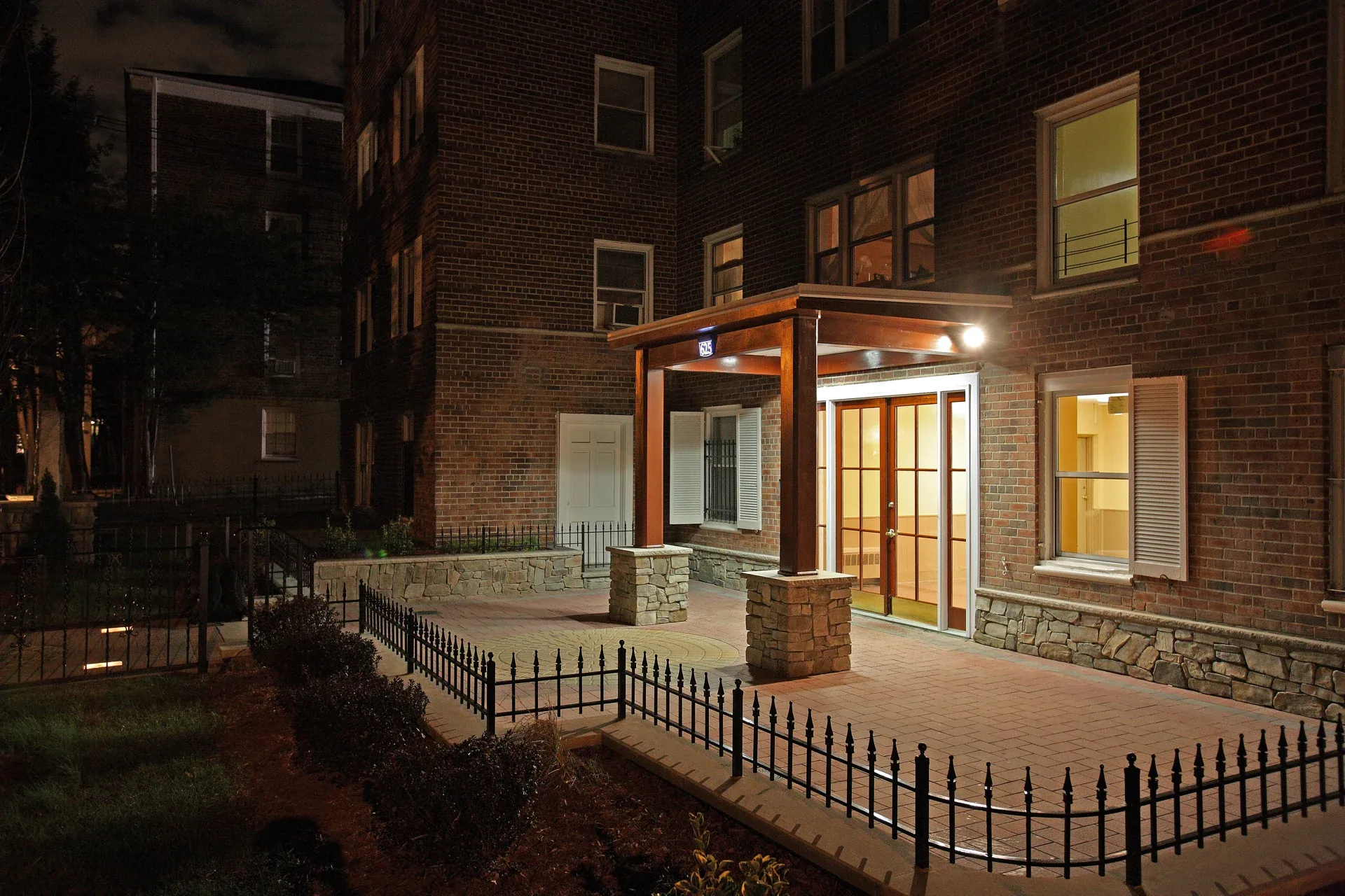 The Colonial: Illuminated entrance canopy with wood posts, stone bases and a paved forecourt