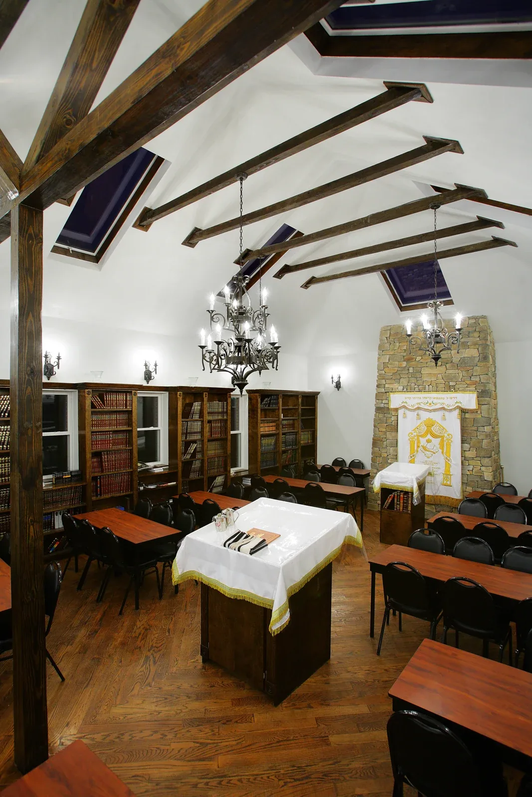 Yeshiva Ateres Shimon: Interior hall with exposed wood beams, skylights, chandeliers and rows of tables